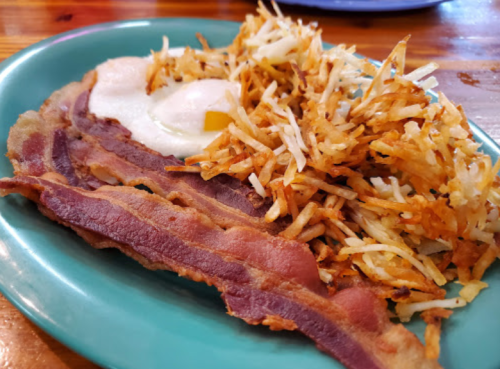 A plate of crispy bacon, golden hash browns, and a sunny-side-up egg on a green dish.
