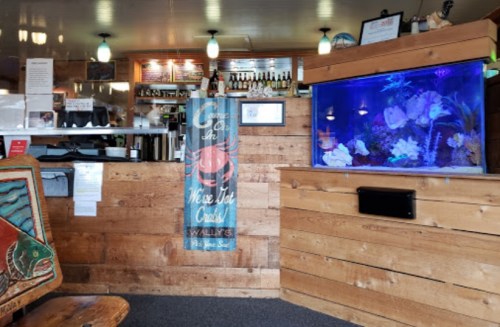 Interior of a cozy restaurant featuring a wooden bar, an aquarium, and a welcoming sign.