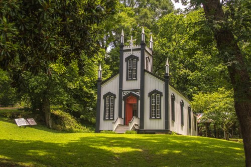 A small, black and white church with a red door, surrounded by lush green trees and grass.