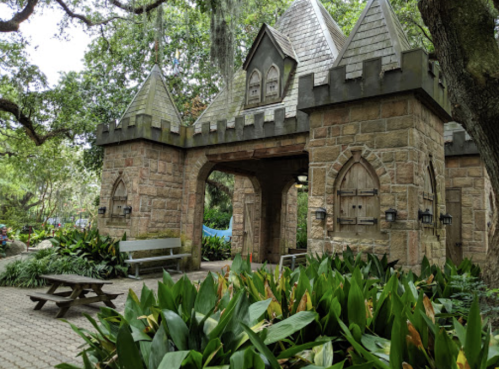 A stone castle entrance surrounded by lush greenery and benches in a park setting.