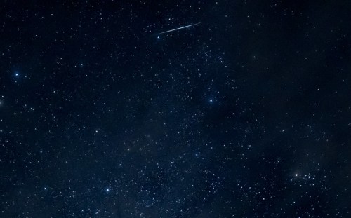 A starry night sky filled with countless stars and a bright meteor streaking across the scene.