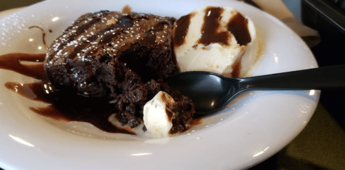 A rich chocolate brownie with a scoop of vanilla ice cream drizzled with chocolate sauce on a white plate.