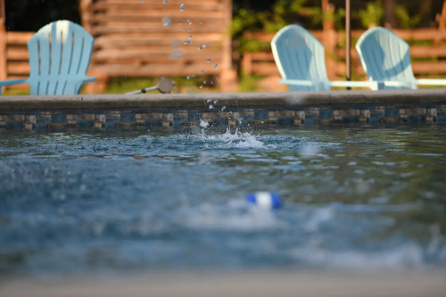 A pool with splashes of water and a blue and white ball floating, surrounded by empty blue chairs.