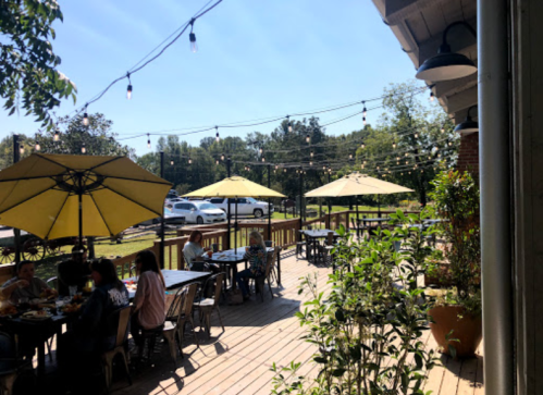 Outdoor dining area with yellow umbrellas, string lights, and patrons enjoying meals on a sunny day.