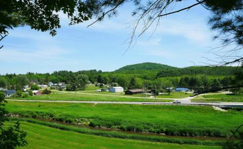 A scenic view of a green landscape with a small town, hills in the background, and a winding stream.