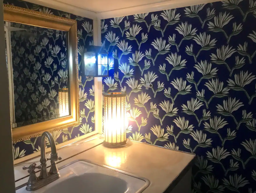 A bathroom with a floral blue wallpaper, a mirror, a sink, and a lantern providing warm light.