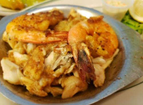 A metal plate filled with shrimp and fish, lightly seasoned and cooked, garnished with lemon and a side of coleslaw.