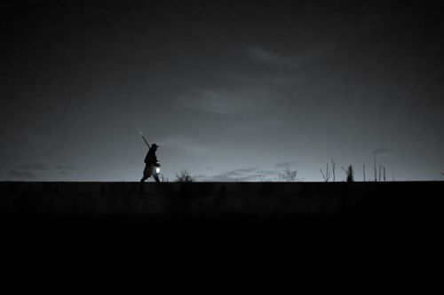 A silhouette of a fisherman walking at night, holding a lantern against a dark sky.