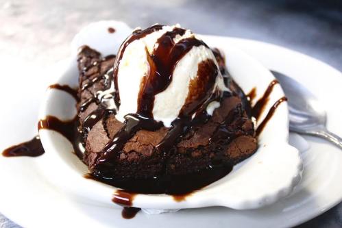 A warm brownie topped with vanilla ice cream and drizzled with chocolate sauce, served in a white dish.