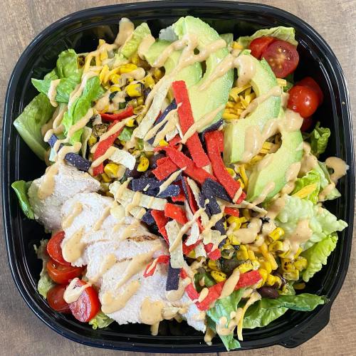 A colorful salad with lettuce, grilled chicken, avocado, cherry tomatoes, corn, black beans, tortilla strips, and dressing.