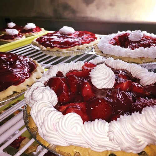A close-up of several strawberry pies topped with whipped cream, displayed on a refrigerator shelf.