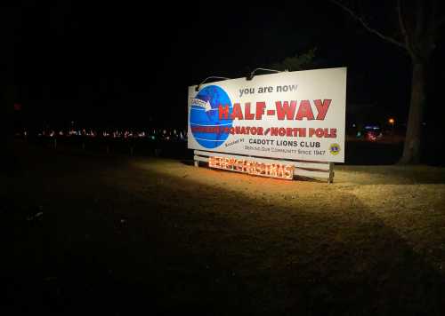 Sign reading "You are now halfway between the Equator and North Pole" at Cadott Lions Club, illuminated at night.