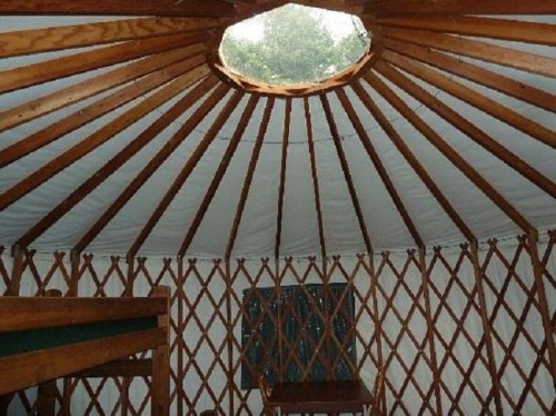 Interior of a yurt featuring wooden beams, a circular skylight, and a cozy, rustic atmosphere.