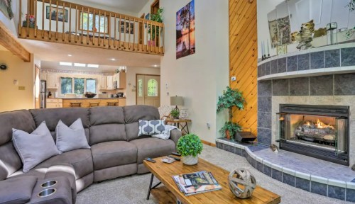 Cozy living room with a fireplace, comfortable sofa, wooden accents, and an open kitchen in the background.
