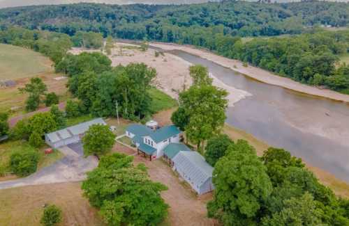 Aerial view of a rural property with a house, outbuildings, and a river surrounded by greenery and hills.