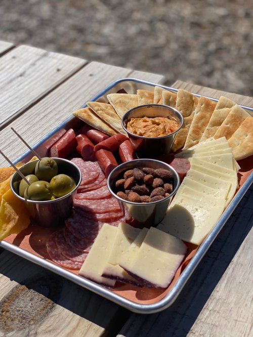 A charcuterie board featuring meats, cheeses, olives, crackers, and dips on a wooden table.