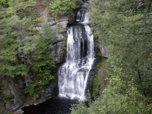 A serene waterfall cascading down rocky cliffs, surrounded by lush green trees and a tranquil pool below.