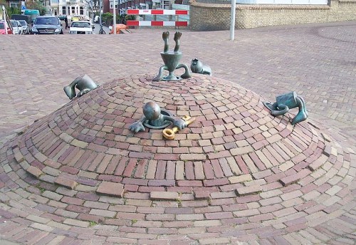 A whimsical bronze sculpture on a brick mound featuring playful figures, including a child with a flute and animals.