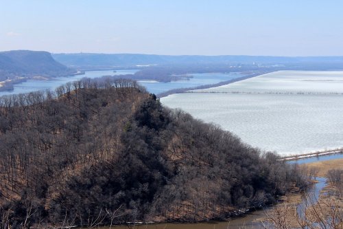 A scenic view of a river winding through a landscape with hills and patches of ice on the water.