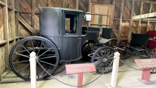 A vintage Drough Coach from circa 1905 displayed in a wooden barn, with a sign asking not to touch.