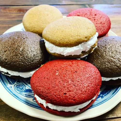 A plate of colorful whoopie pies in red, brown, and yellow, filled with white cream.