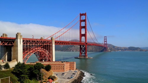 Golden Gate Bridge spans a bay under a clear blue sky, with green hills in the background and calm waters below.