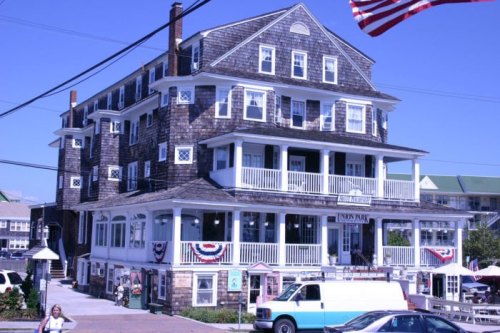 Historic wooden hotel with multiple balconies, American flags, and decorative bunting, set in a coastal town.