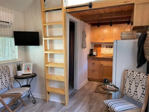 Cozy interior of a tiny home featuring a ladder, kitchenette, and seating area with natural light.