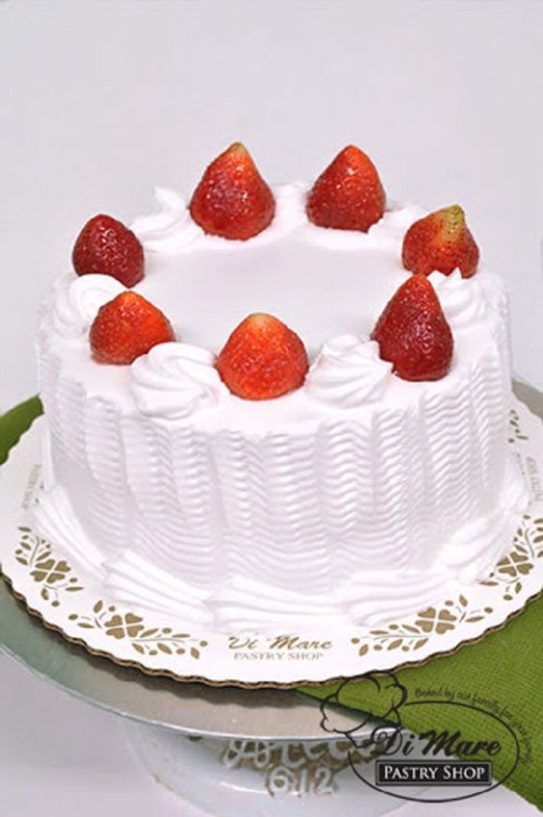 A round white cake topped with fresh strawberries and decorative whipped cream, displayed on a cake stand.