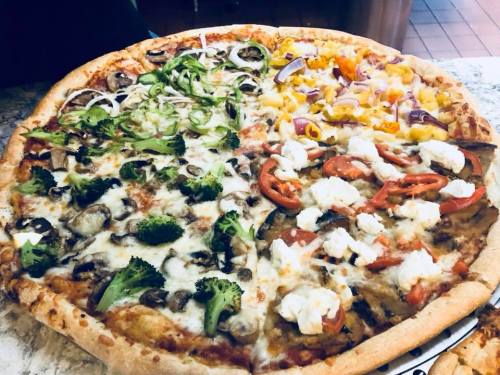 A large pizza divided into four sections, topped with vegetables like broccoli, mushrooms, peppers, and cheese.
