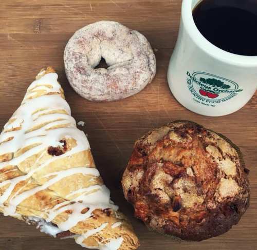 A wooden surface with a croissant, a cinnamon donut, a muffin, and a cup of coffee.