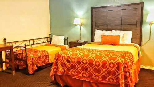 A cozy hotel room featuring two beds with orange patterned bedspreads, a nightstand, and soft lighting.