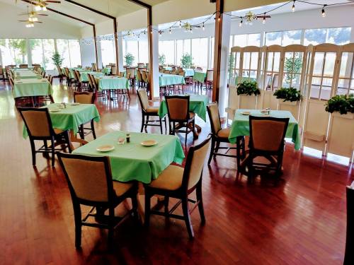 A spacious restaurant with green tablecloths, wooden chairs, and large windows letting in natural light.