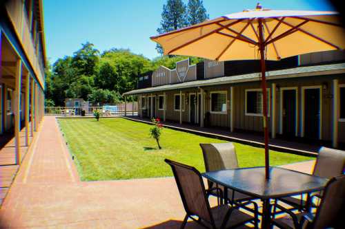 A sunny courtyard with a table and umbrella, surrounded by rooms and greenery.