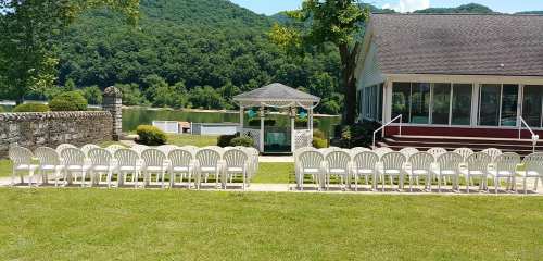 A row of white chairs set up for an outdoor event near a gazebo, with a scenic view of green hills and a lake.
