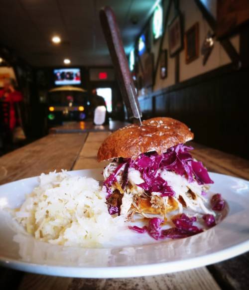 A close-up of a pulled pork sandwich with purple cabbage on a plate, accompanied by a side of sauerkraut.