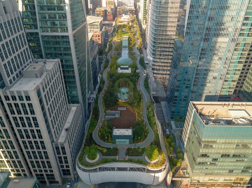 Aerial view of a green urban park surrounded by tall buildings, featuring pathways and landscaped areas.