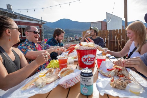 A group of friends enjoying seafood and drinks at an outdoor table with mountains in the background.