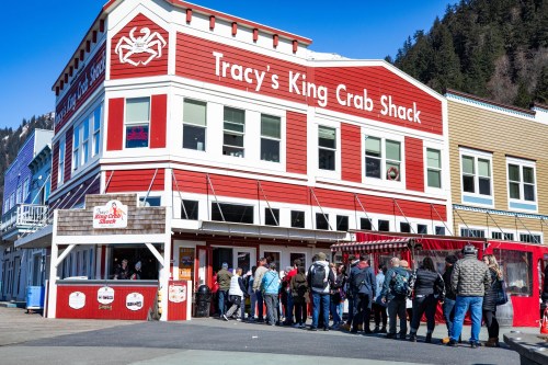 A busy seafood restaurant, Tracy's King Crab Shack, with a line of customers outside on a sunny day.