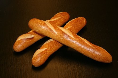 Three freshly baked baguettes arranged in a cross on a dark surface.