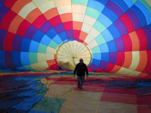 A person walks inside a colorful hot air balloon, surrounded by vibrant fabric patterns in red, blue, green, and yellow.