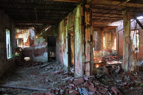 An abandoned, dilapidated interior with crumbling walls, scattered debris, and broken windows.