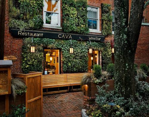 A cozy restaurant entrance with greenery on the walls, wooden seating, and warm lighting.