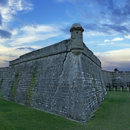 Historic stone fort with a rounded tower, set against a dramatic sky and green grass.