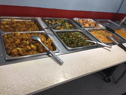 A buffet table with various dishes, including vegetables, rice, and samosas, served in metal trays with serving utensils.