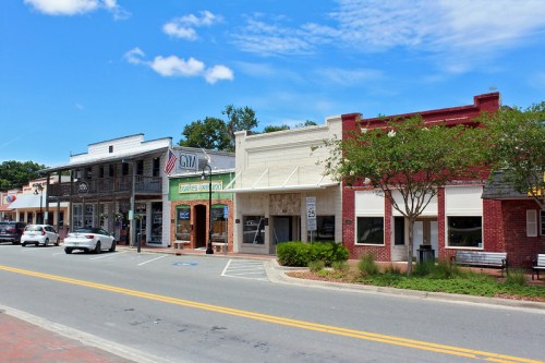A charming street view of small-town shops with trees and blue skies in the background.