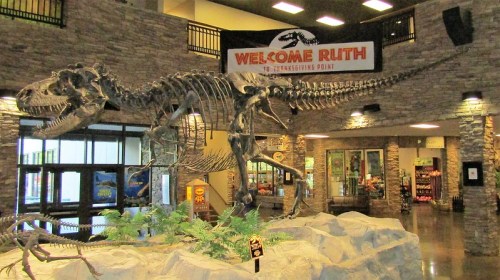 A large dinosaur skeleton on display in a stone-walled lobby, with a "Welcome to Ruth" banner above.