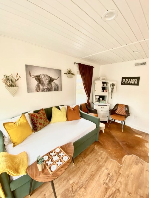 Cozy room with a green sofa, colorful pillows, a bull portrait, and a small desk, featuring warm wood accents.