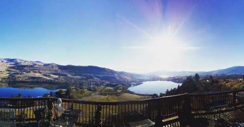 A panoramic view of a serene landscape with lakes, hills, and a bright sun shining in a clear blue sky.