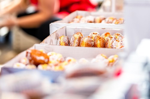 A close-up of boxes filled with assorted donuts, some dusted with powdered sugar, at a market or fair.